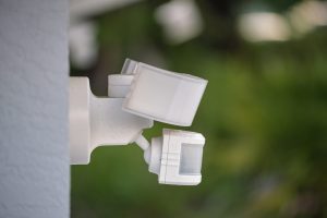 Motion sensor with light detector mounted on exterior wall of private house as part of security system.